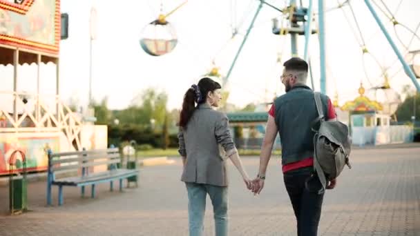 Un paio di passeggiate nel parco divertimenti. Hipster uomo e donna alla moda andare a cavalcare su ruota panoramica. Fidanzato e fidanzata si divertono in vacanza. — Video Stock