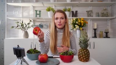 Yemek blogcusu mutfak stüdyosunda taze meyve salatası pişiriyor video kanalı için özel ders kameraları önünde çekim yapıyor. Kadın nüfuzlu kişi elmayı, ananası tutuyor ve sağlıklı beslenmekten bahsediyor. Fructorianism