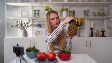 Yemek blogcusu mutfak stüdyosunda taze meyve salatası pişiriyor video kanalı için özel ders kameraları önünde çekim yapıyor. Kadın nüfuzlu kişi elmayı, ananası tutuyor ve sağlıklı beslenmekten bahsediyor. Fructorianism