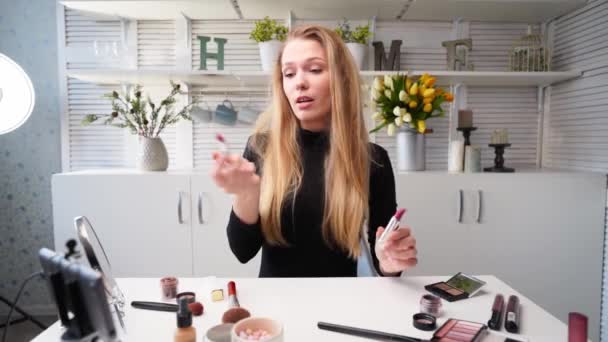 Vlogger samice nanáší rtěnku na rty. Krása blogger žena natáčení denní make-up rutinní návod na kameru na stativ. Influencer blondýny dáma live streaming kosmetika srovnání produktů ve studiu — Stock video