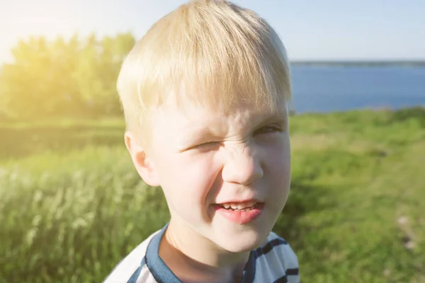 うれしそうな金髪の少年の肖像画と自然で太陽から彼の目を閉じて. — ストック写真