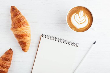 Kapuçino, iki ay çöreği ve defter.