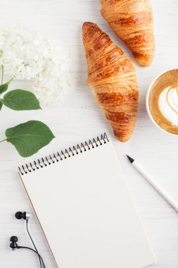 Kapuçino, iki ay çöreği ve defter.