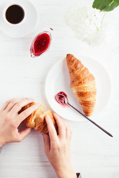 Manos sosteniendo croissant sobre la mesa . — Foto de Stock
