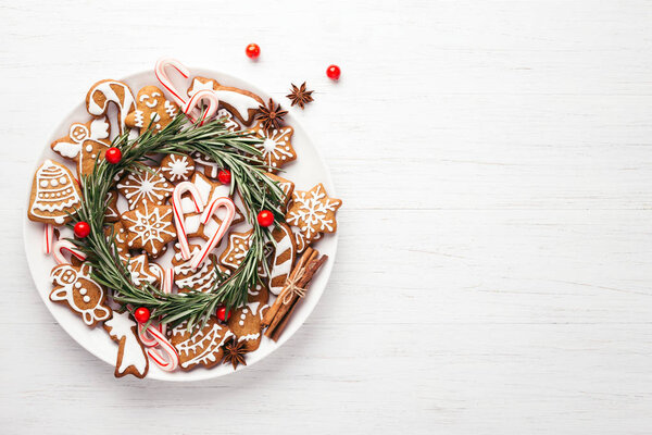 Plate with Christmas gingerbread cookies decorated with wreath made of rosemary on white table. Top view, copy space.