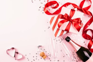 Kırmızı kurdele, şampanya, süslemeleri ile pembe arka plan üzerinde iki bardak hediye kutuları. Güzel Noel ve Sevgililer kompozisyon ile parıldıyor. Arka plan kopya alanı ile.