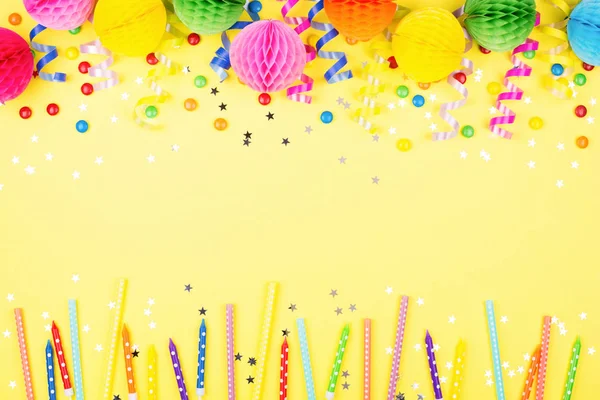 Birthday party background on yellow. Top view. Border made of colorful serpentine, balls and candies.