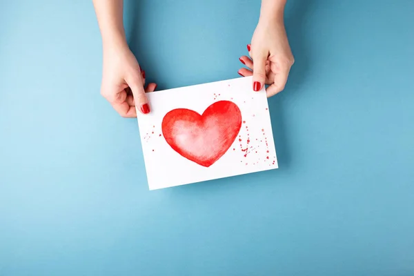 Руки женщины держат карточку с сердцем на синем фоне . — стоковое фото