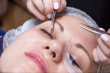 Bir güzellik uzmanı, bir kadının gözüne cımbız ve yapıştırıcıyla kirpik takıyor. Kadın uzanıyor ve gözleri kapalı..