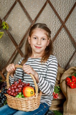 At kuyruklu neşeli bir kız bir ahırda elinde renkli meyvelerle oturuyor. Gülümsemesi sıcacık ve doğrudan izleyiciye bakıyor. Kırsal ahşap çitler sahneye cazibe katıyor..