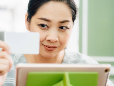 Mutlu Asyalı kadın tablete online alışveriş için beyaz mockup kredi kartı ile.