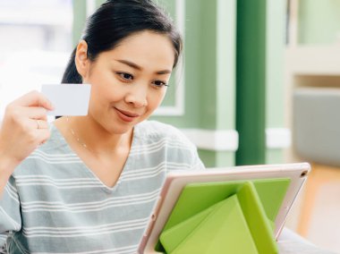 Mutlu Asyalı kadın tablete online alışveriş için beyaz mockup kredi kartı ile.