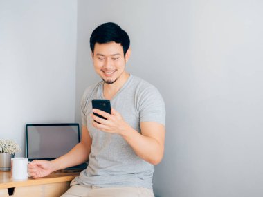 Mutlu ve smile Asya adam akıllı telefon ev ofisinde kullanıyor.