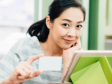 Mutlu Asyalı kadın tablete online alışveriş için beyaz mockup kredi kartı ile.