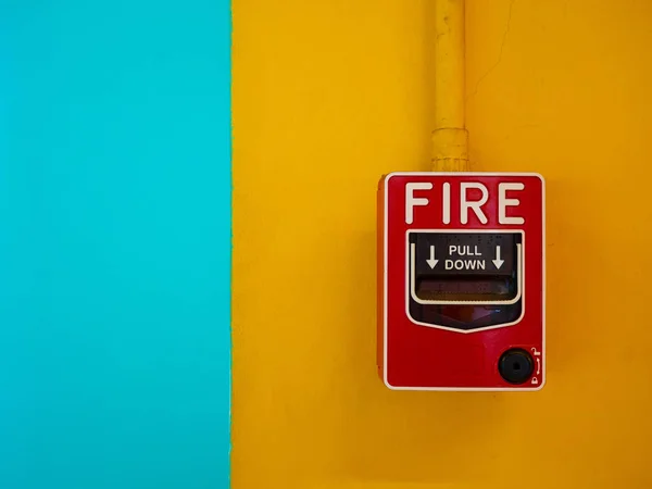 Red manual fire alarm activation switch mounted on yellow wall.