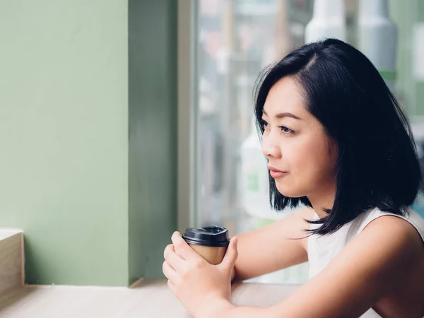 Asian woman is drinking a hot cup of coffee and sit by the windows.