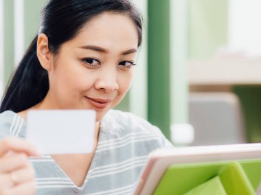 Mutlu Asyalı kadın tablete online alışveriş için beyaz mockup kredi kartı ile.