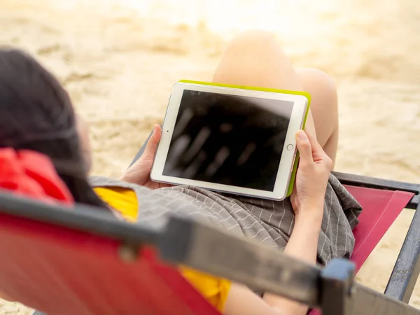 stock image Asian woman relax on beach bed and play with the tablet.