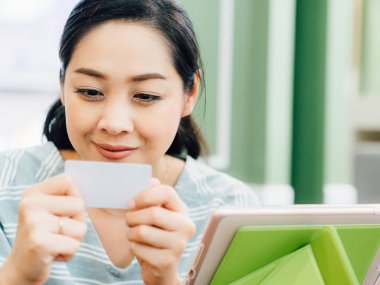 Mutlu Asyalı kadın tablete online alışveriş için beyaz mockup kredi kartı ile.