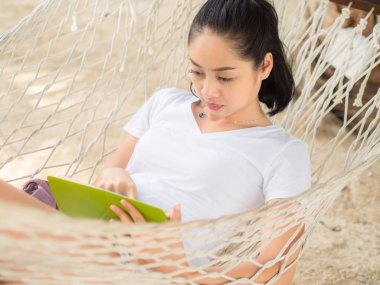 Asyalı kadın kullanarak tablet ve hamak Tayland sahilde dinlenin.