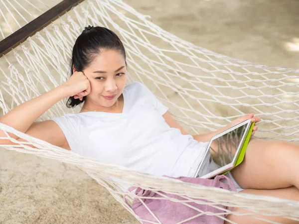 Asyalı kadın kullanarak tablet ve hamak Tayland sahilde dinlenin.