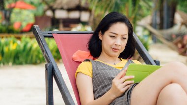 Asyalı kadın kullanım tablete yaz plaj tatil sırasında.