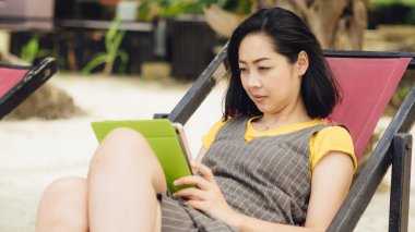 Asyalı kadın kullanım tablete yaz plaj tatil sırasında.