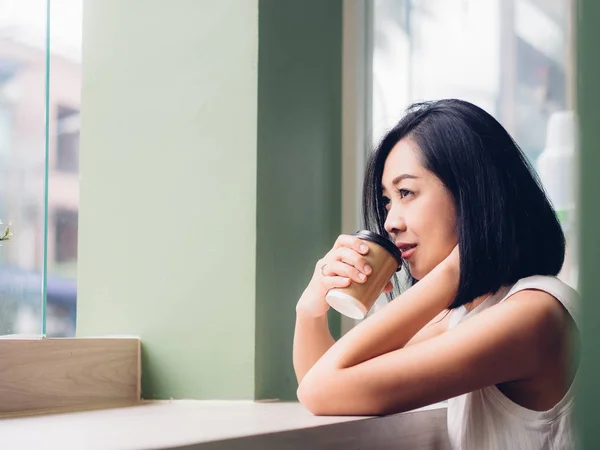 Asian woman is drinking a hot cup of coffee and sit by the windows.