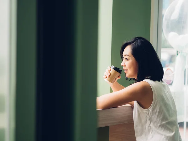 亚洲女人正在喝一杯热咖啡 坐在窗边 — 图库照片