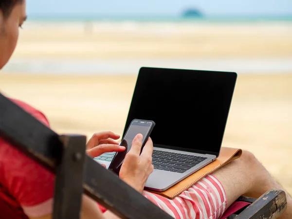 Man relax on camp bed and working online while on vacation at the beach in Thailand.