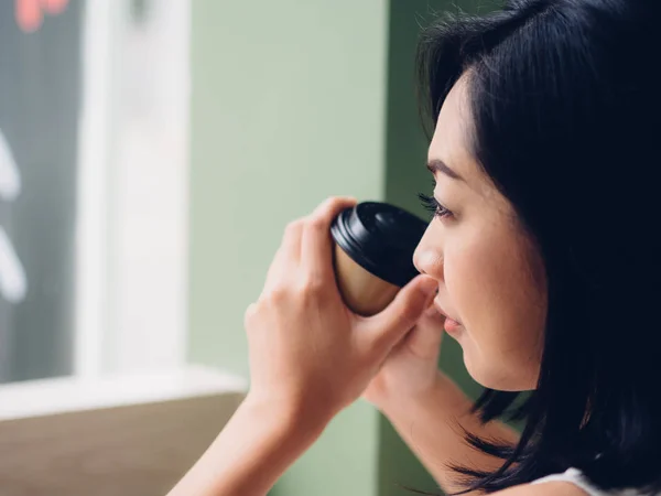 Happy Asian woman is drinking hot cup of coffee in peaceful atmosphere.