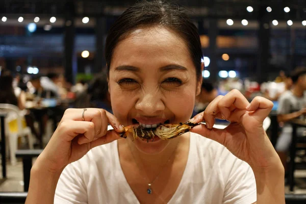 Happy Asian woman eat grilled shrimp with a delicious bite face.