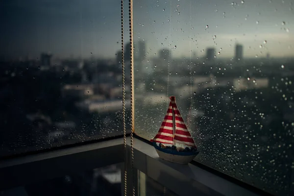Small sailboat on the edge of rainy windows with a bit of sunlight.
