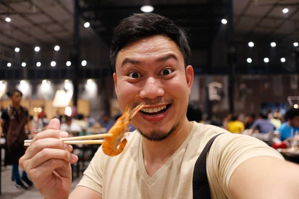 Happy Asian man eat grilled shrimp with chopsticks.