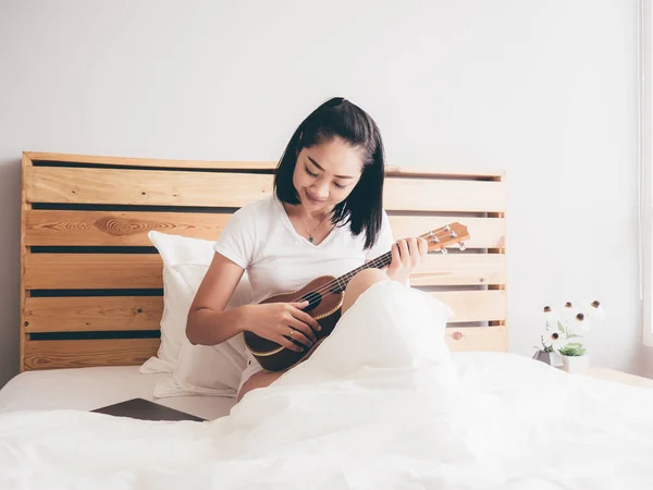 亚洲妇女在她的床上演奏四弦琴在早晨 — 图库照片