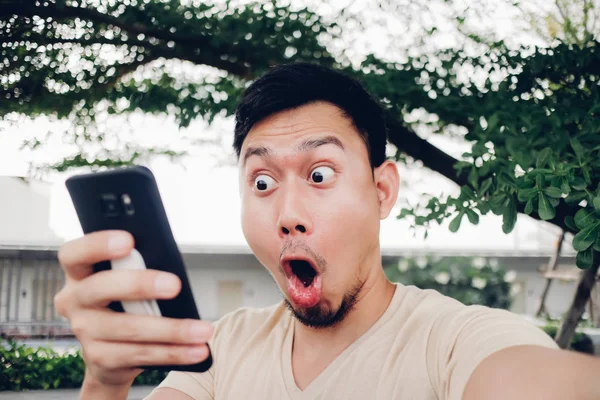 Surprise and shock face of Asian man look at his smartphone.