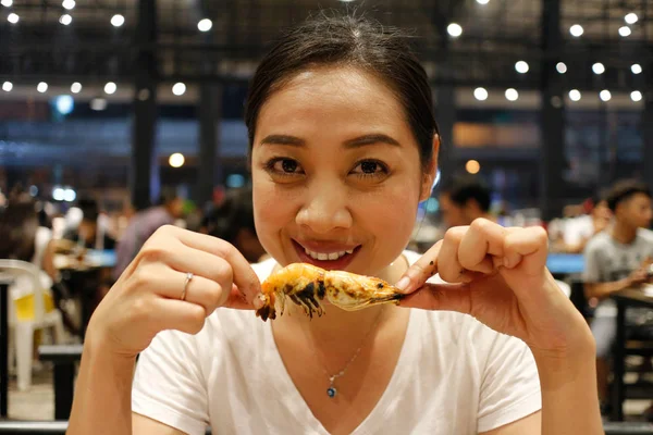 Happy Asian woman eat grilled shrimp with a delicious bite face.
