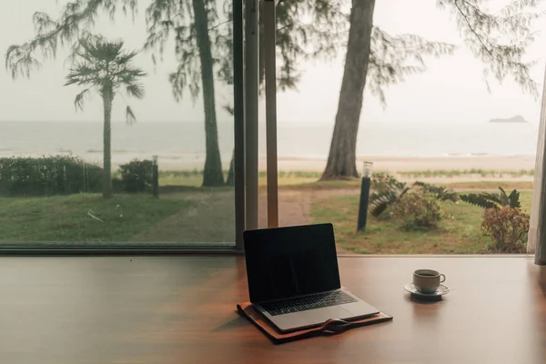 Concept of work and relax. Laptop and hot coffee cup at door step with autumn beach view.