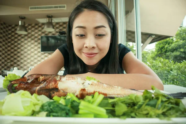 Happy Asian woman with wow face look at grilled fish.