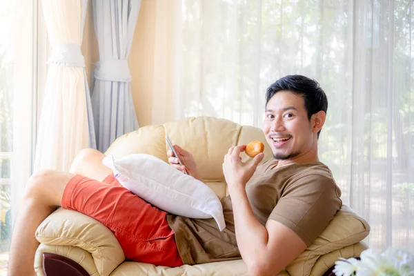 Feliz Ásia Homem Comer Cookies Sofá — Fotografia de Stock