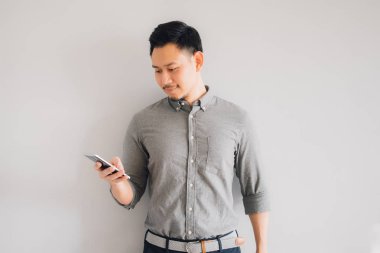 Yakışıklı Asyalı adamın mutlu gülümseme yüzünü kullanın gri arka plan üzerinde izole smartphone standı.