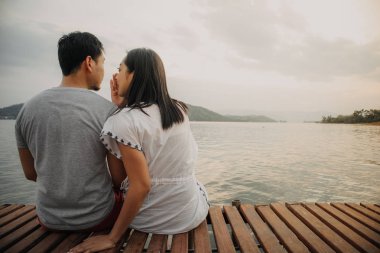 Romantik Asyalı çift fısıldıyor ve göl manzarasının tadını çıkarıyor.