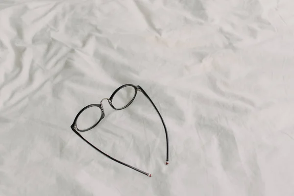 Brille mit schwarzem Kunststoffbügel auf weißem Bettlaken. — Stockfoto
