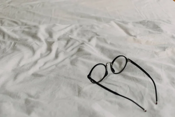 Beyaz çarşaf üzerinde siyah plastik tapınak ile Gözlük. — Stok fotoğraf