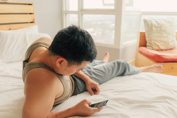 Asiático hombre mentira en cama y relajarse en su apartamento en calidez domingo verano primavera . — Foto de Stock