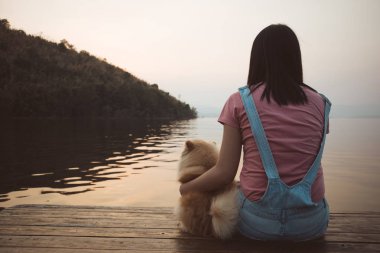 Kadın köpeğiyle oturur ve dinlenir. Gün batımına ve göle hayran kalır..