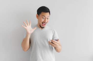 Gri tişörtlü adamın yüzü akıllı telefondan şaşırıyor..