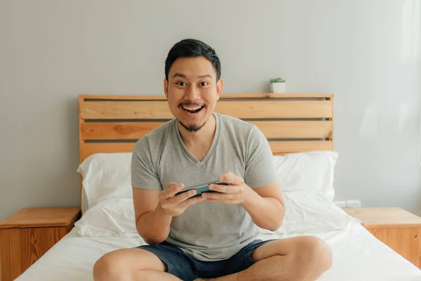 Homem está jogando jogo móvel com seu smartphone na cama . — Fotografia de Stock