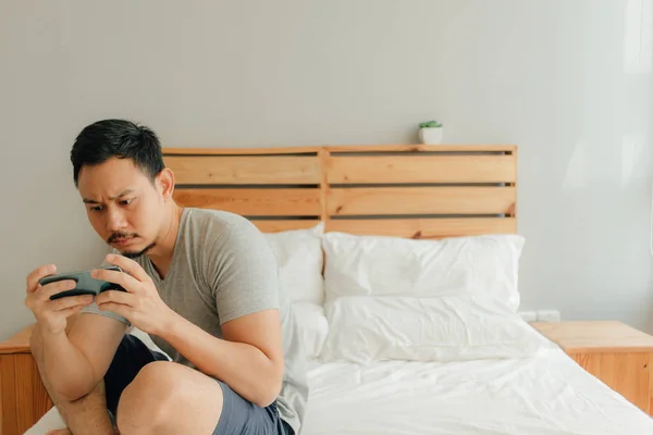 Homem está jogando jogo móvel com seu smartphone na cama . — Fotografia de Stock