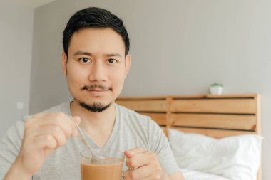 Adam yatak odasında yatakta bir fincan kahve içiyor..